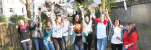 Eine Gruppe von Jugendlichen springt in die Höhe und wirft dabei Zeitungsaritkel fröhlich in die Luft.