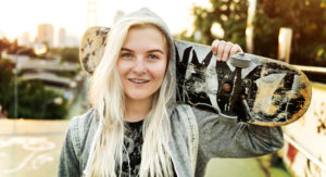 Blondes Mädchen mit Hoodie und Skateboard in der Hand