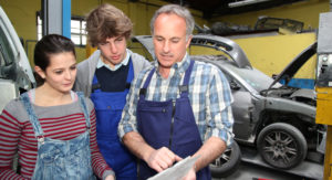 2 Jugendliche in einer Autowerkstatt erhalten von einen Ausbildner eine erklärung