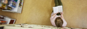 Jugendliche sitzt am Boden in einer Bibliothek und liest ein Buch