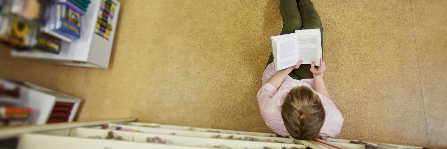 Jugendliche sitzt am Boden in einer Bibliothek und liest ein Buch