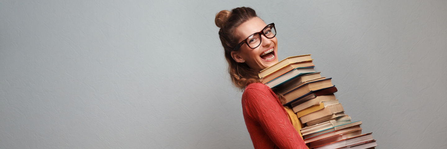 Junges Mädchen fröhlich mit ganz vielen Büchern am Tragen